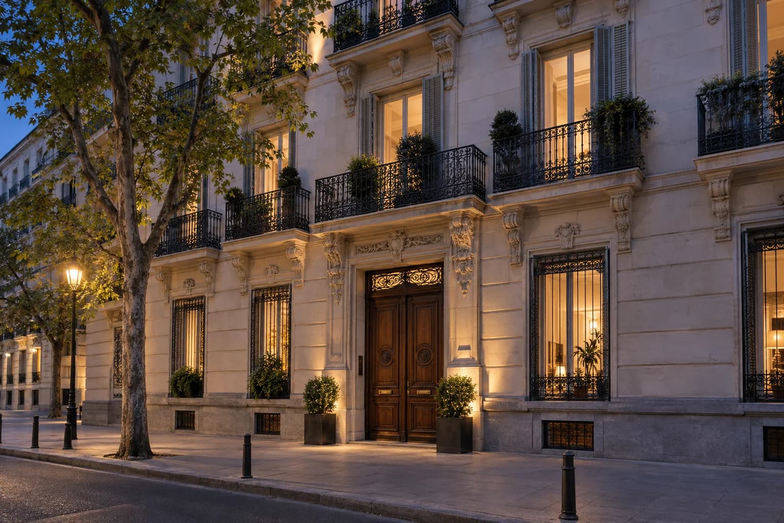 An elegant Madrid residential facade with iron balconies and warmly lit windows at dusk.